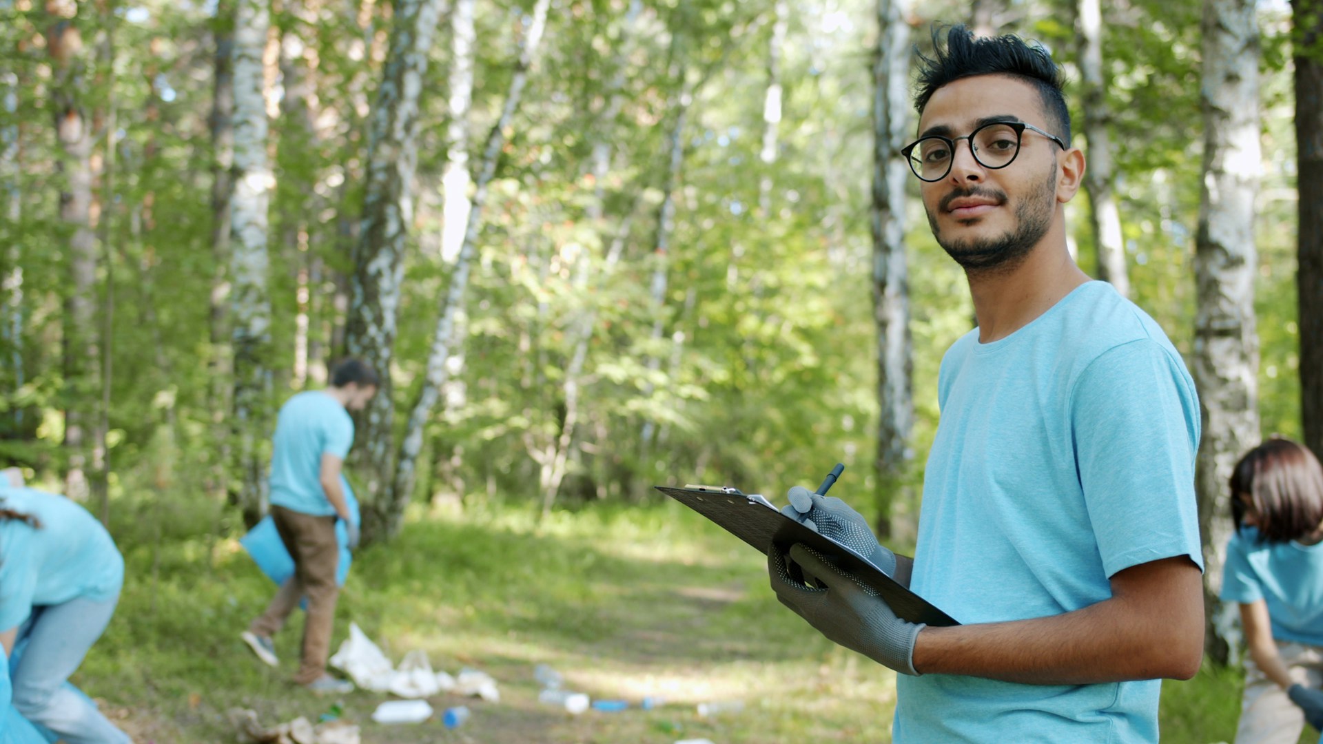 Volunteer in gloves and a team T-shirt holding a clipboard during a forest clean-up