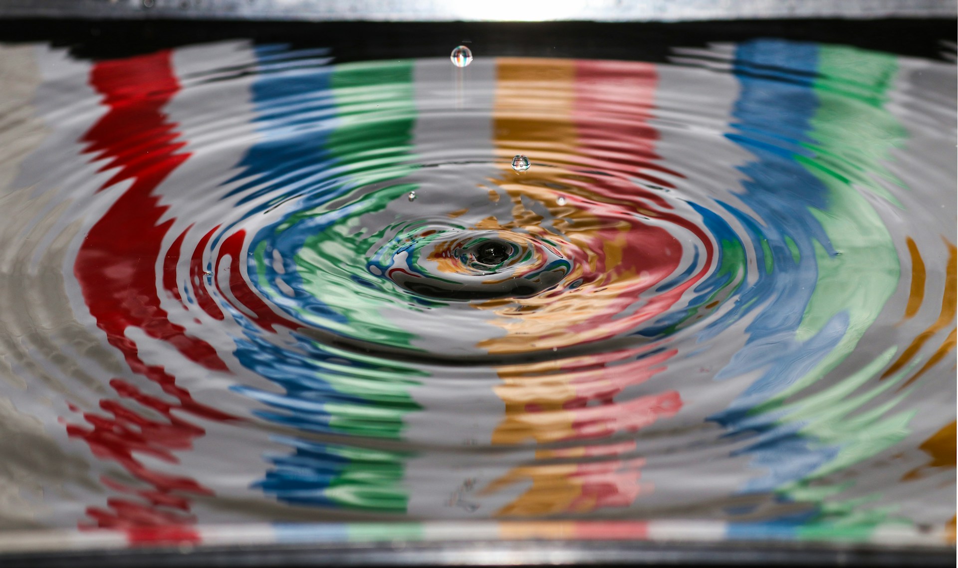 Ripples spreading outwards from a water droplet, reflecting bands of red, blue, green and orange